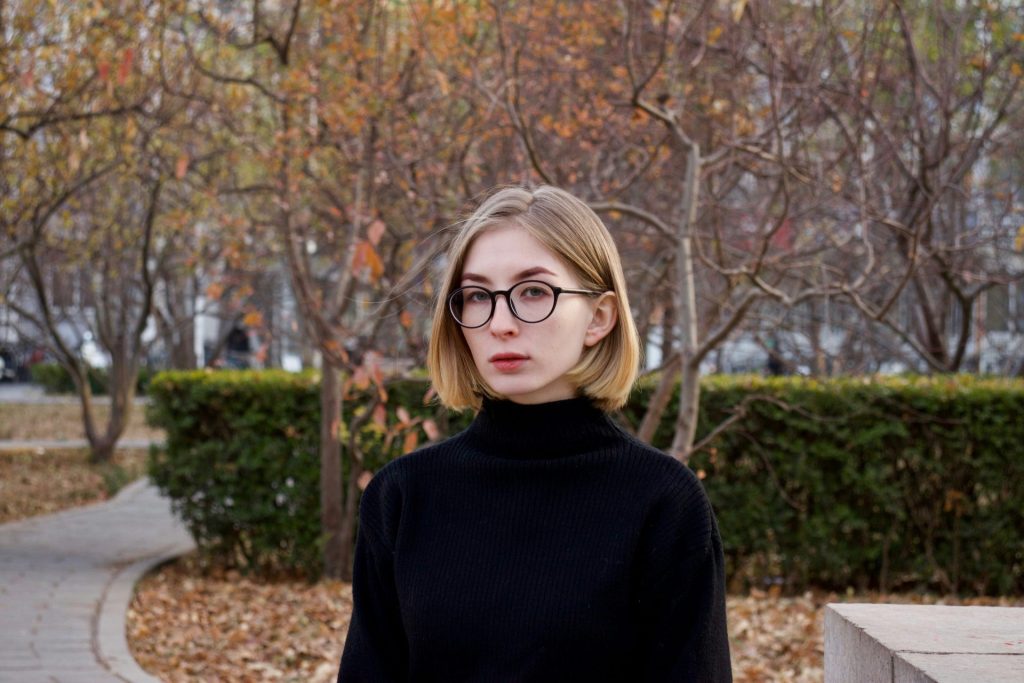 woman in black turtleneck sweater wearing eyeglasses standing near brown bare trees during daytime